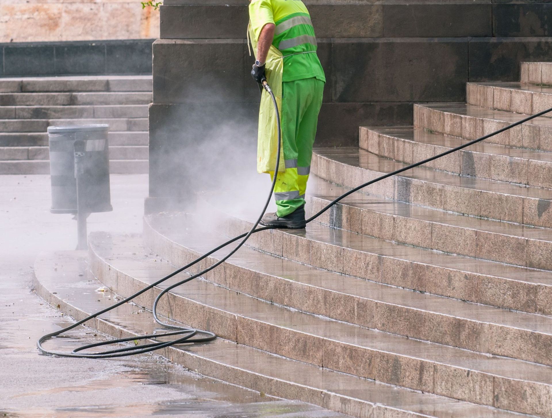 A street worker pressure washes stone stairs in a public park, ensuring cleanliness and safety.